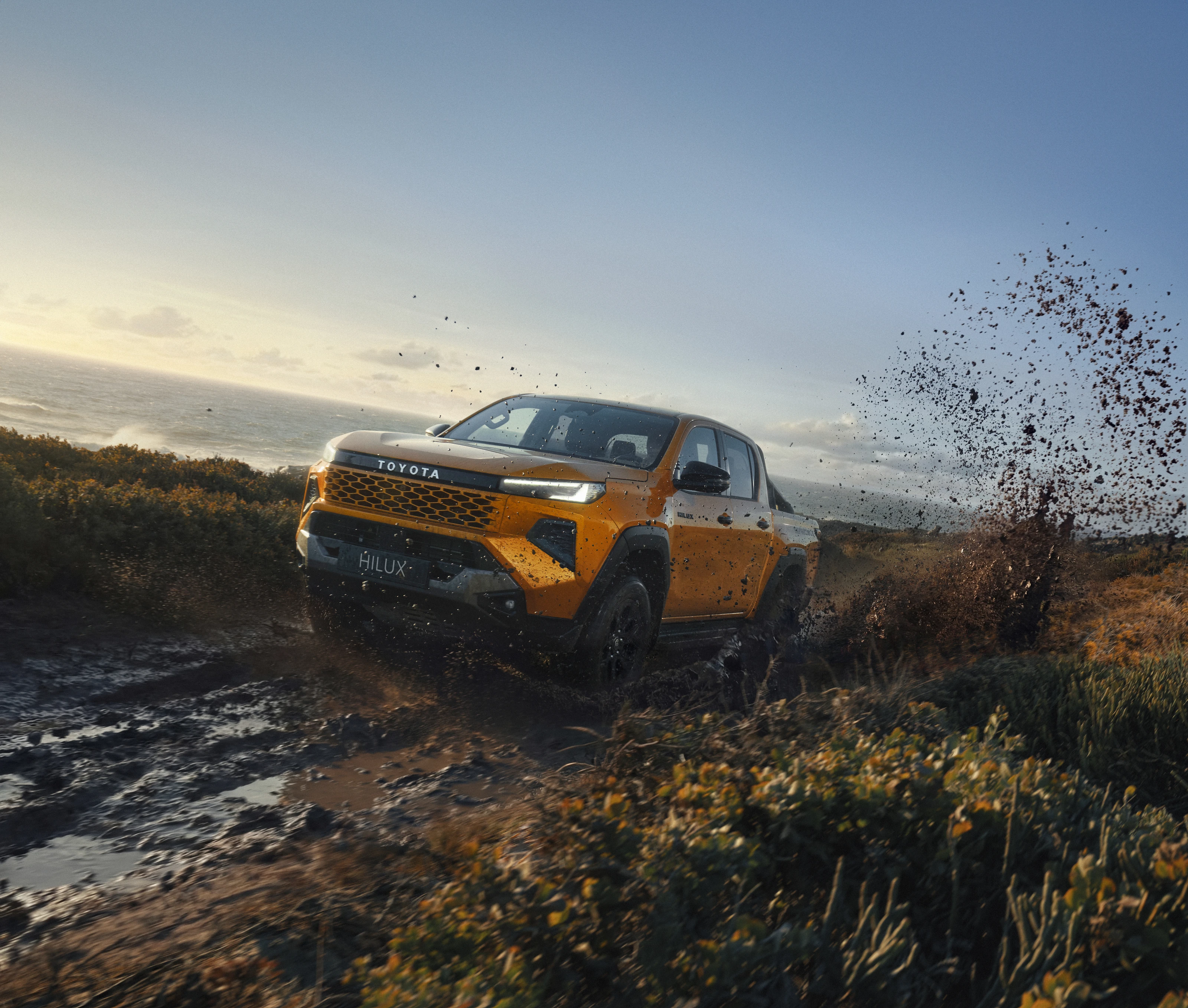 Gold Toyota Hilux throwing mud on a coastal track