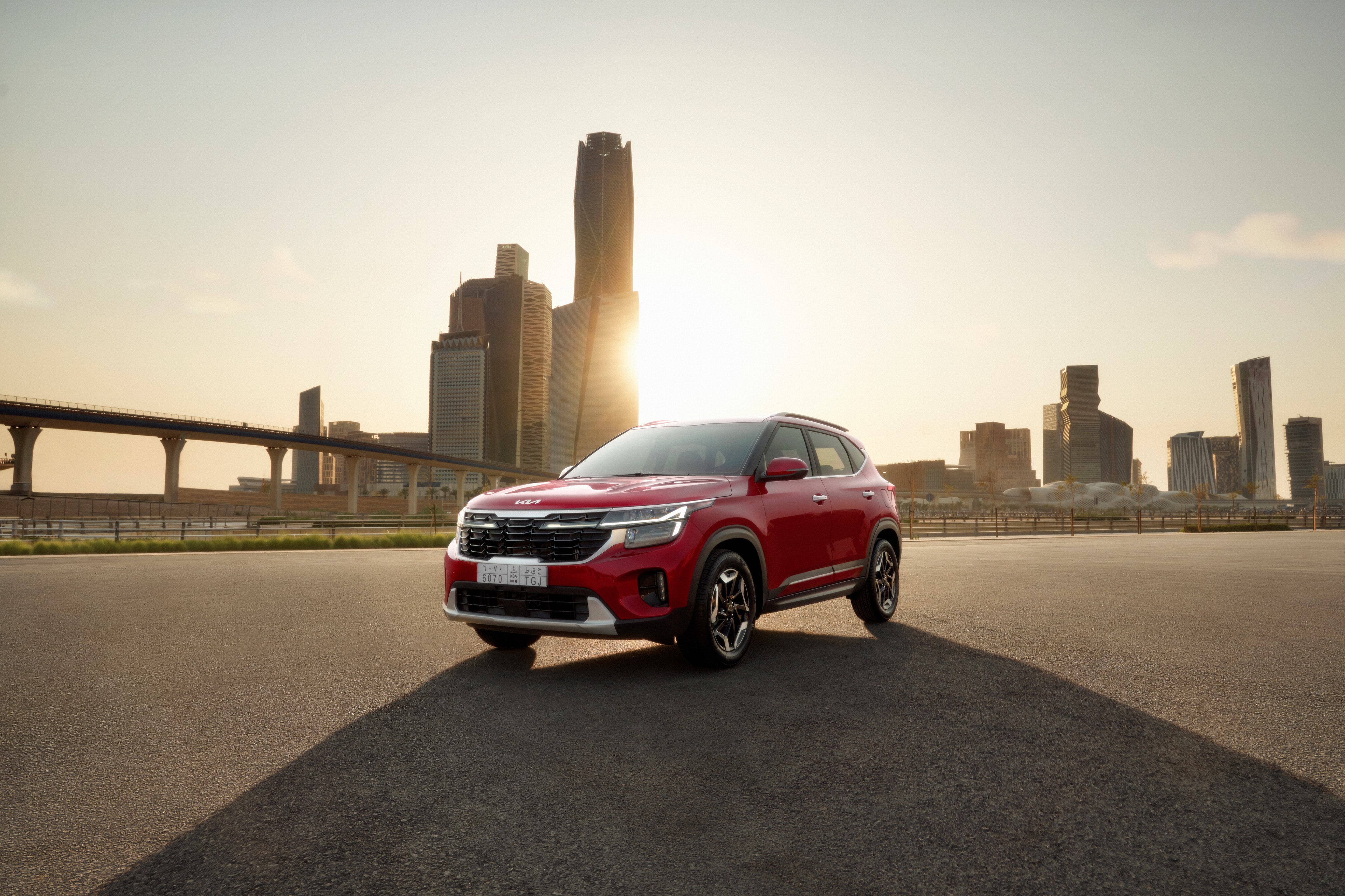 Red KIA Seltos on an open road with a city skyline in warm sunlight